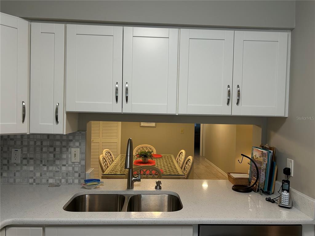 A kitchen sink with white cabinets and a mosaic tile backsplash overlooks a dining area — 5662 GARDENS DRIVE UNIT 104, SARASOTA, FL