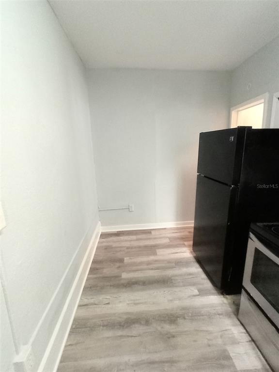 A kitchen area with light gray walls, wood-look flooring, a black refrigerator, and a stove — 704 CORDOVA DRIVE, ORLANDO, FL