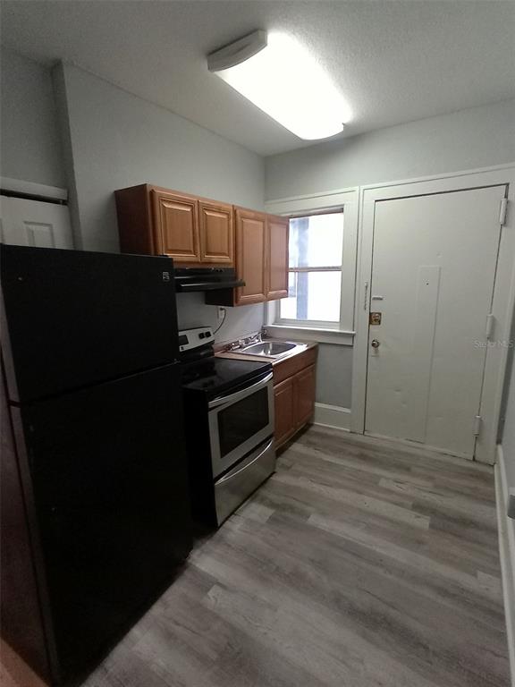 A kitchen features a black refrigerator, stainless steel stove, wood cabinets, and light-colored flooring — 704 CORDOVA DRIVE, ORLANDO, FL