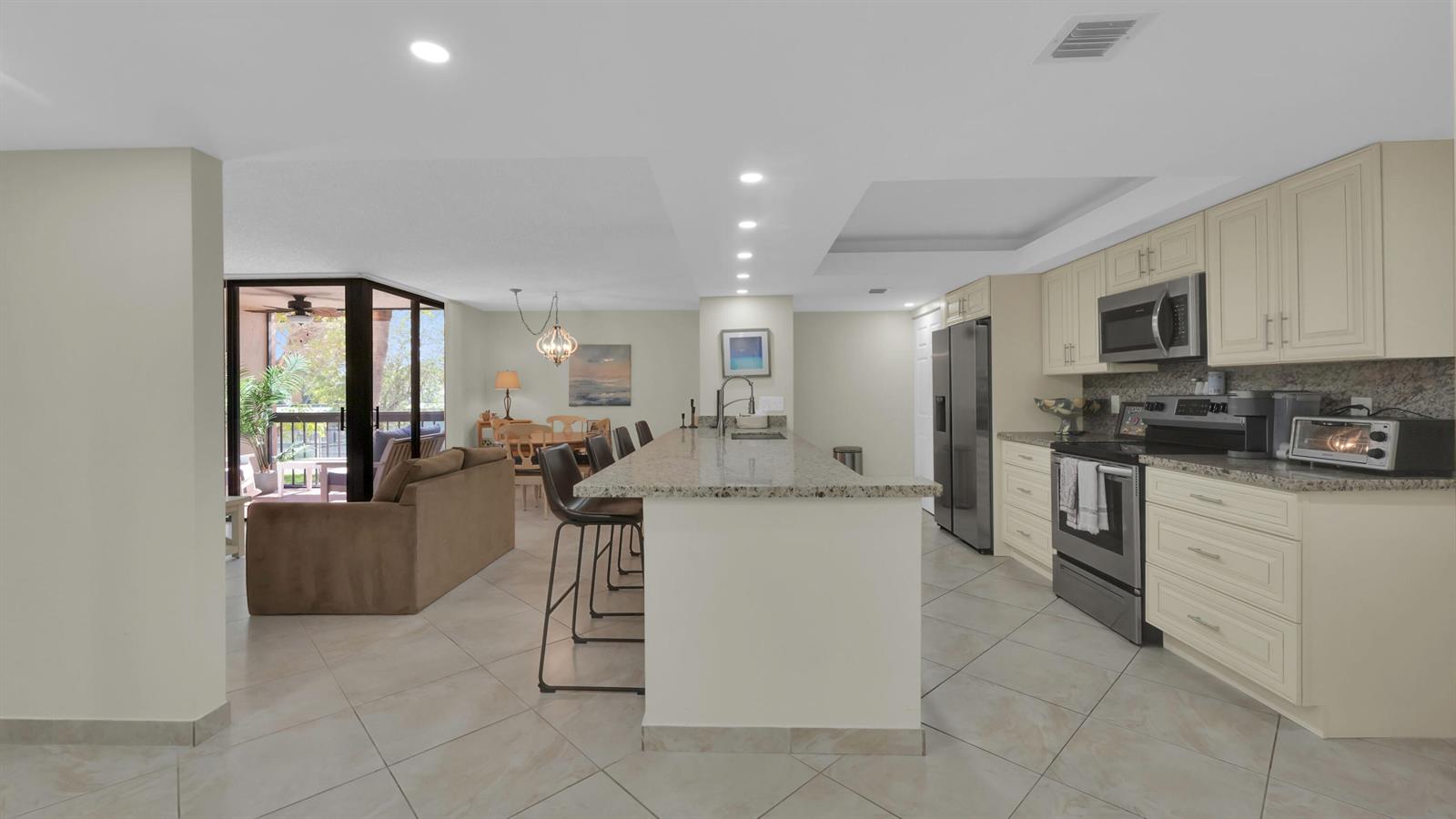 An open-concept kitchen with granite countertops and a breakfast bar overlooks a living area — 450 Egret Circle # 9207, Delray Beach FL 33444, DELRAY BEACH, FL