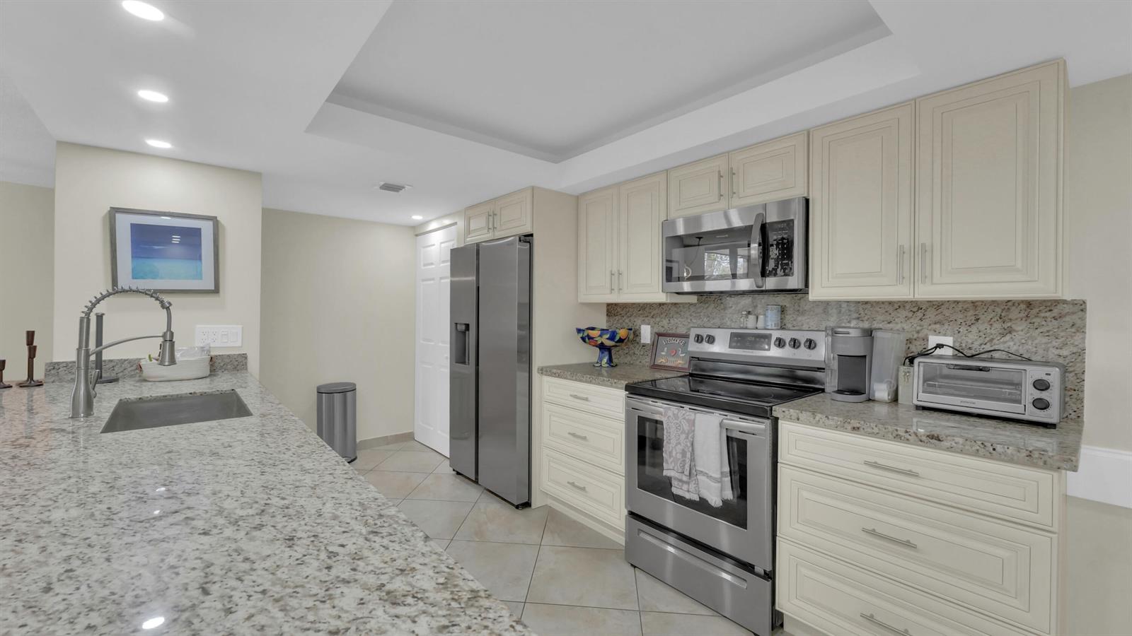 A kitchen features granite countertops, stainless steel appliances, and off-white cabinetry — 450 Egret Circle # 9207, Delray Beach FL 33444, DELRAY BEACH, FL