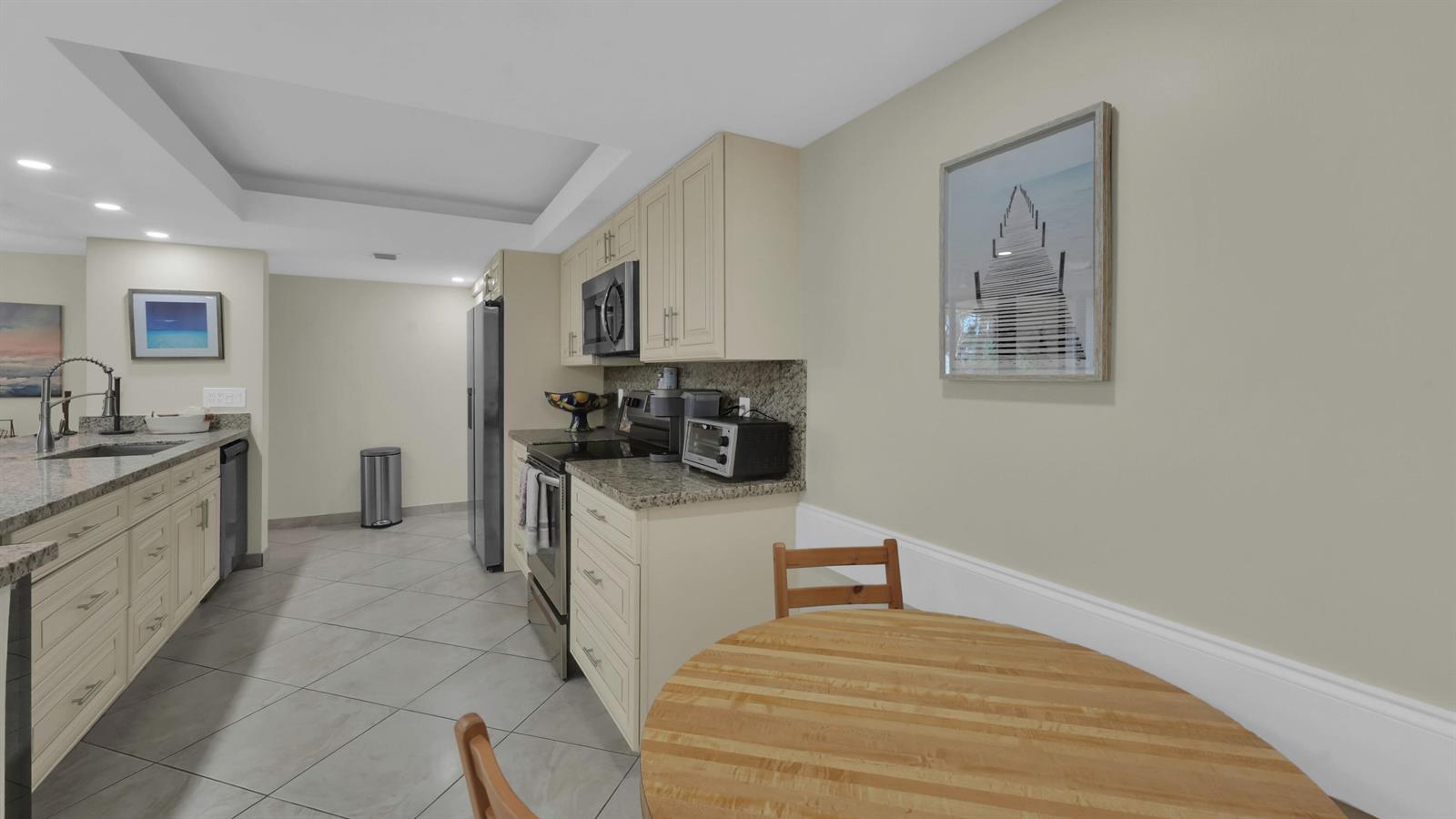 A kitchen features light-colored cabinets, granite countertops, tile flooring, and a small wooden dining table — 450 Egret Circle # 9207, Delray Beach FL 33444, DELRAY BEACH, FL