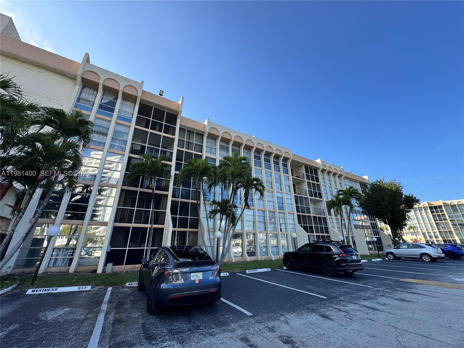A multi-story apartment building with screened balconies and a parking lot in the foreground — 701 Three Islands Blvd # 103, Hallandale Beach FL 33009, HALLANDALE BEACH, FL