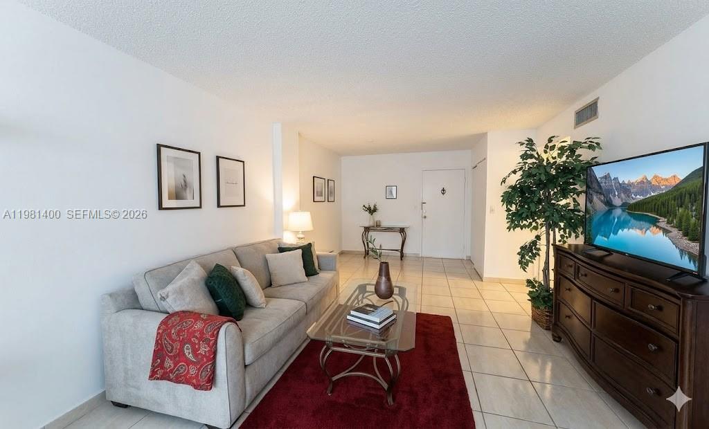 A living room features a gray sofa, a glass coffee table, and a television console — 701 Three Islands Blvd # 103, Hallandale Beach FL 33009, HALLANDALE BEACH, FL