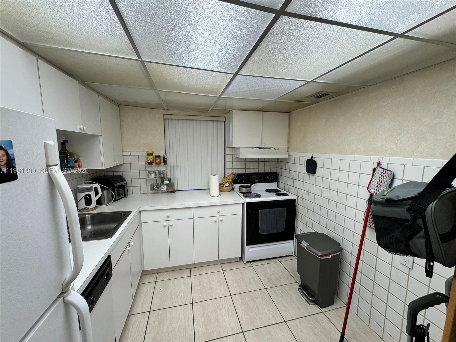 A kitchen features white cabinets, white tile walls, a stove, and a drop ceiling — 701 Three Islands Blvd # 103, Hallandale Beach FL 33009, HALLANDALE BEACH, FL