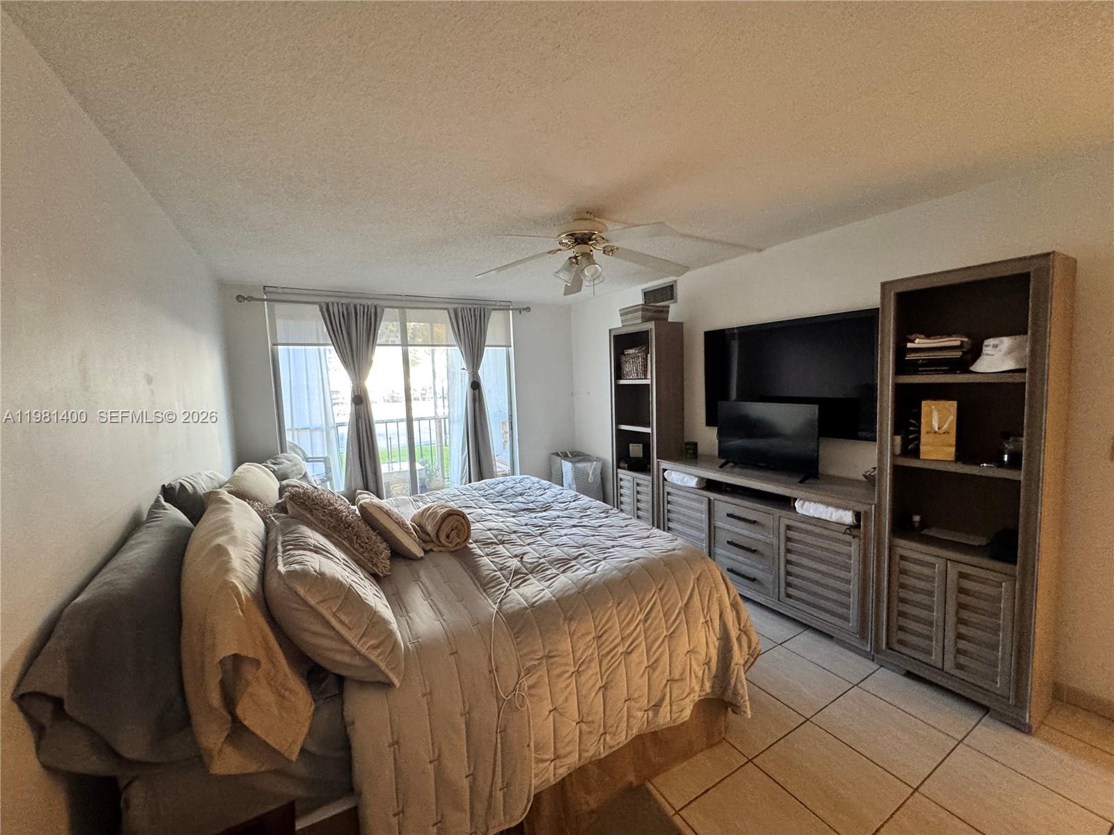 A bedroom features a bed, a large entertainment unit with shelving, and a sliding glass door — 701 Three Islands Blvd # 103, Hallandale Beach FL 33009, HALLANDALE BEACH, FL