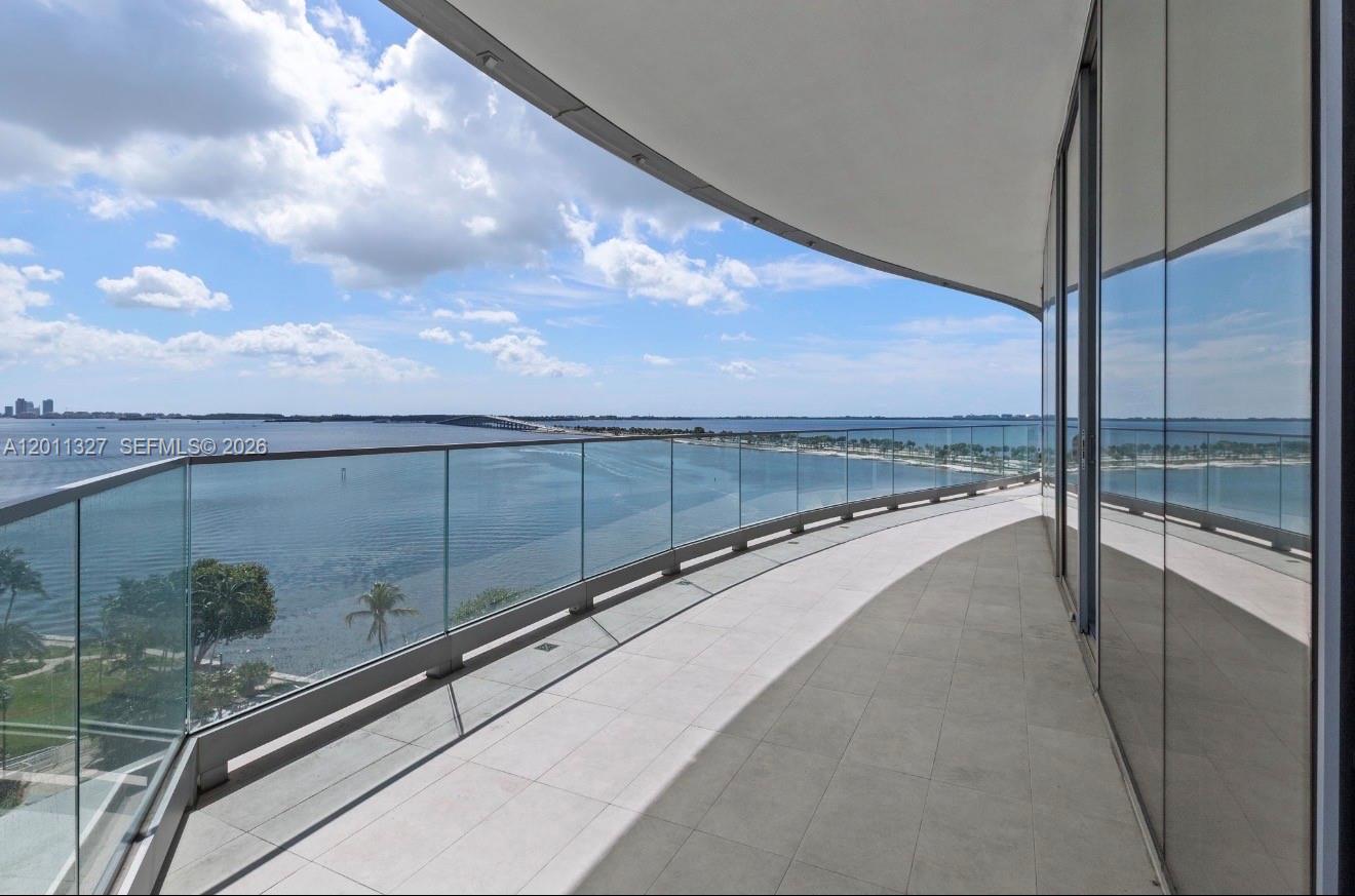 A curved balcony with glass railings overlooks a large body of water and a bridge — 175 SE 25th Rd # 704, Miami FL 33129, MIAMI, FL