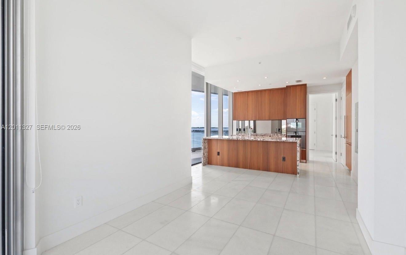 A modern kitchen features wood cabinetry, a granite island, and white tile flooring — 175 SE 25th Rd # 704, Miami FL 33129, MIAMI, FL