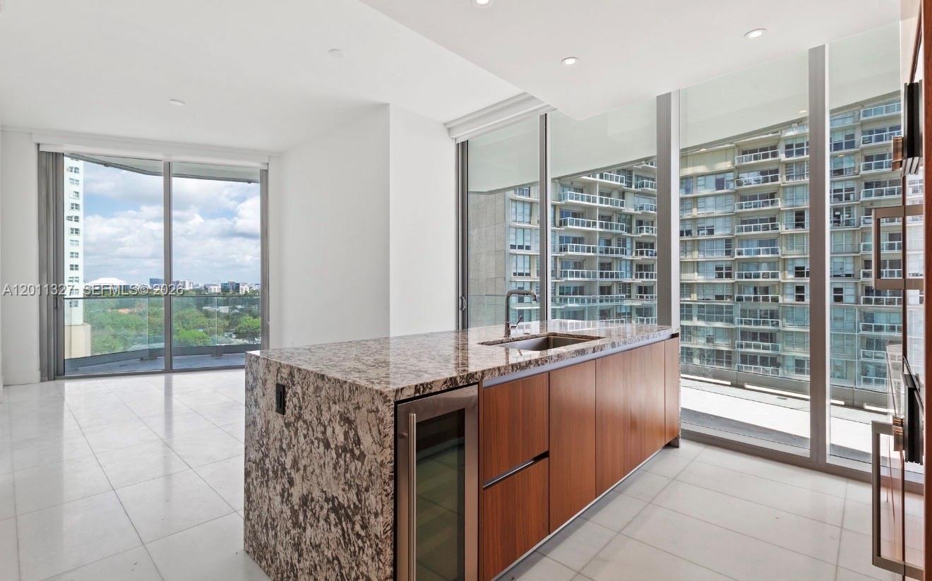 A modern kitchen island with granite countertops and wood cabinetry sits before floor-to-ceiling windows — 175 SE 25th Rd # 704, Miami FL 33129, MIAMI, FL