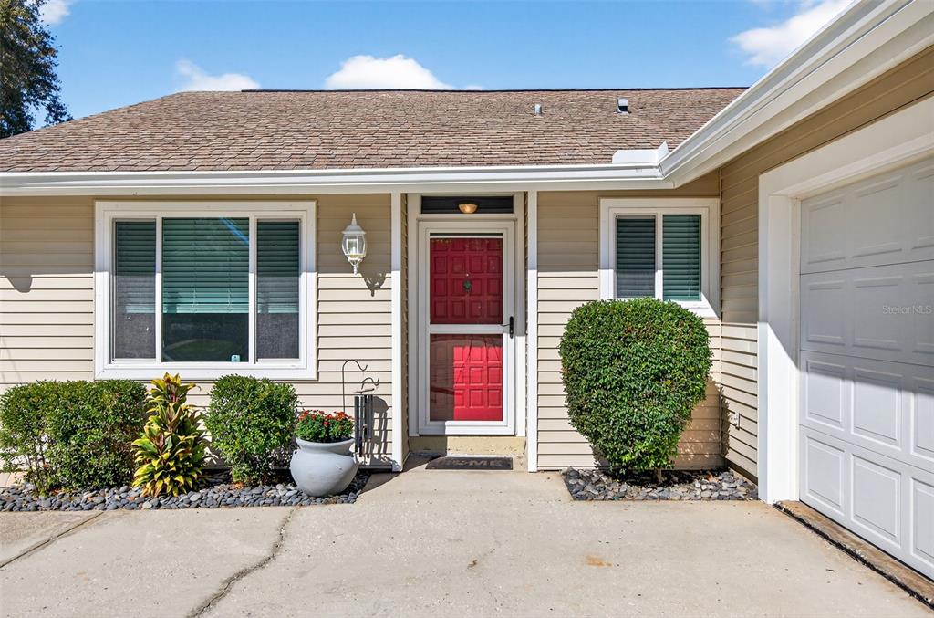 The exterior of a single-story house features beige siding, a red front door, and landscaping — 2366 PEMBROOK DRIVE, CLEARWATER, FL
