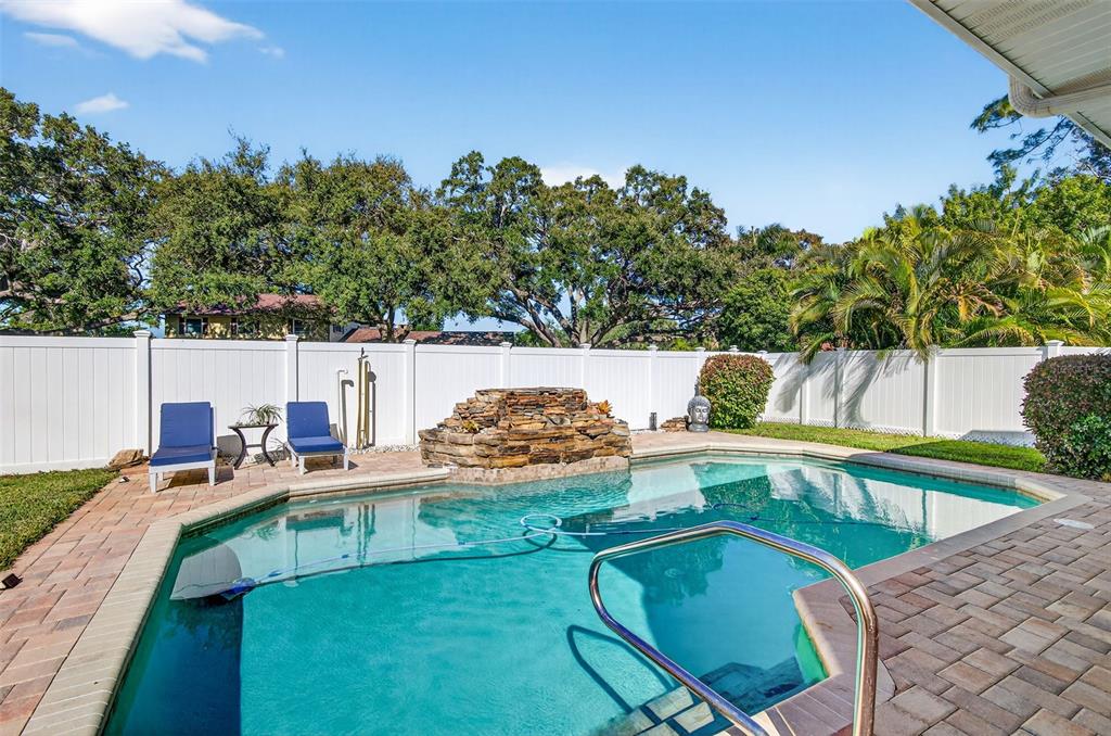 A backyard swimming pool features a stone waterfall, lounge chairs, and a white privacy fence — 2366 PEMBROOK DRIVE, CLEARWATER, FL