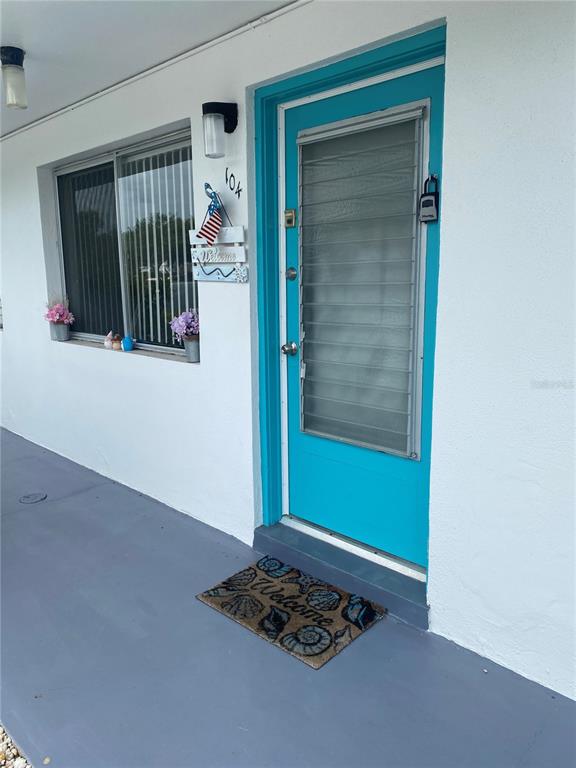 A turquoise front door with a storm door and a welcome mat on a porch — 8350 112TH STREET UNIT 104, SEMINOLE, FL