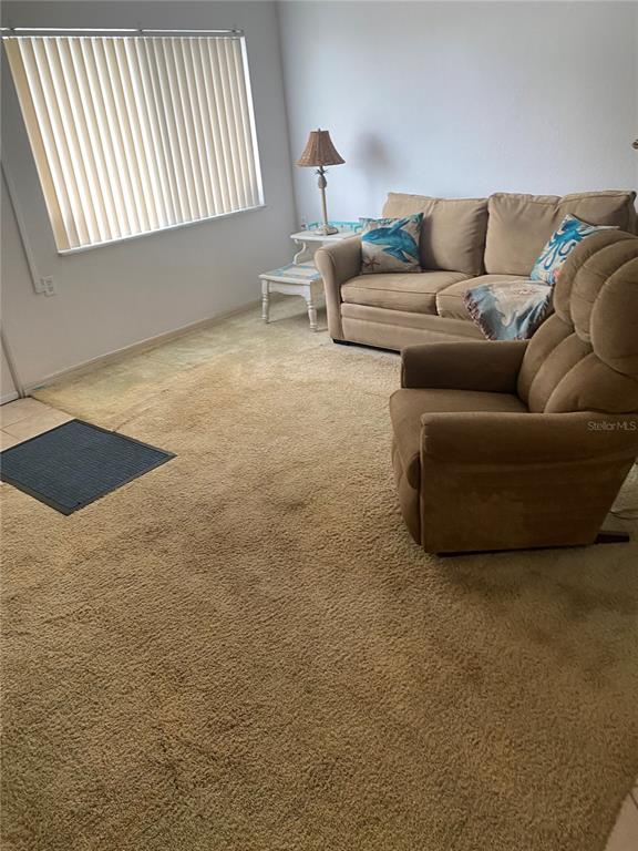 A living room features beige wall-to-wall carpeting, a tan sofa, a recliner, and vertical blinds — 8350 112TH STREET UNIT 104, SEMINOLE, FL