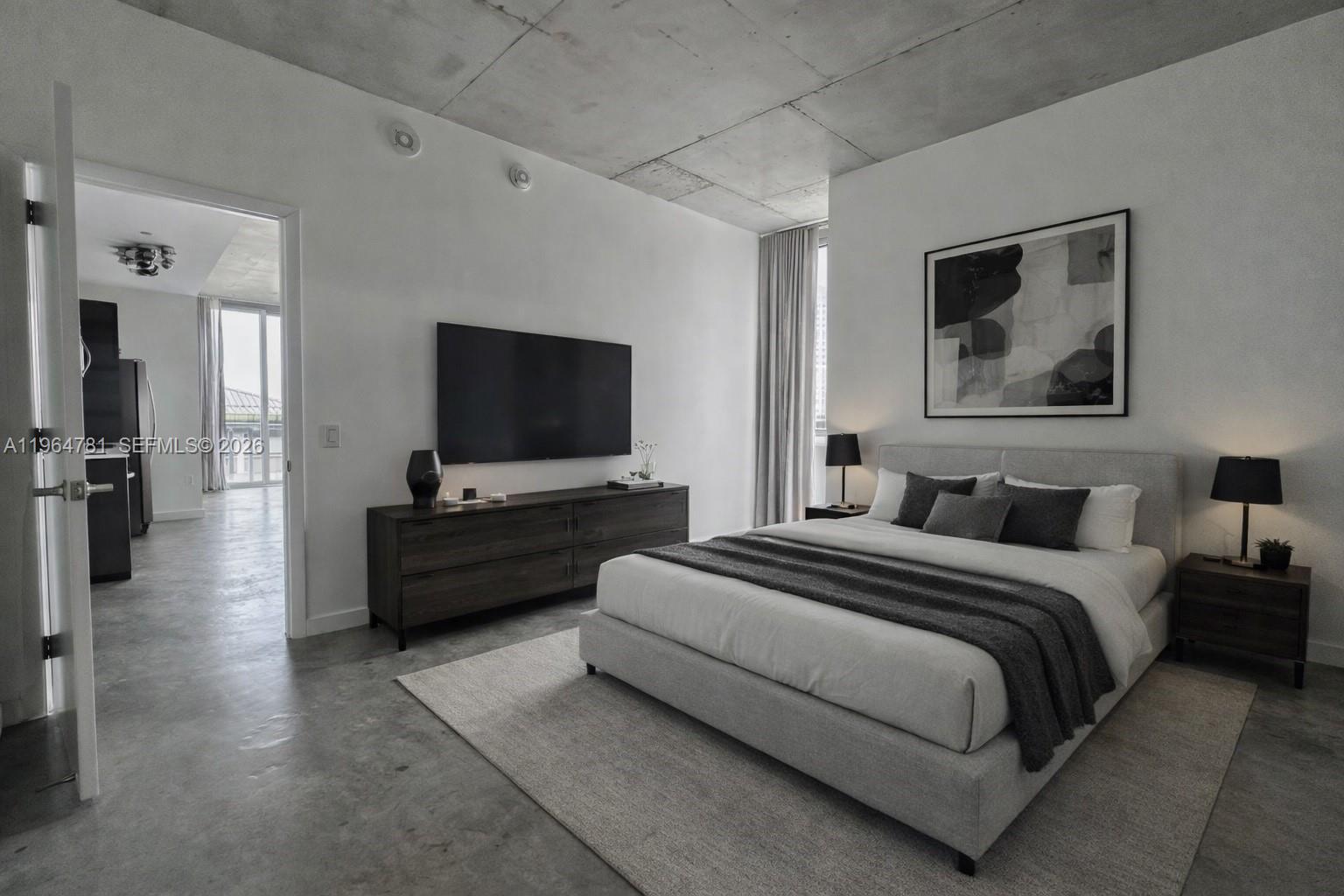 A modern bedroom features a concrete ceiling, gray flooring, a bed, and a wall-mounted television — 151 SE 1st St # 1501, Miami FL 33131, MIAMI, FL