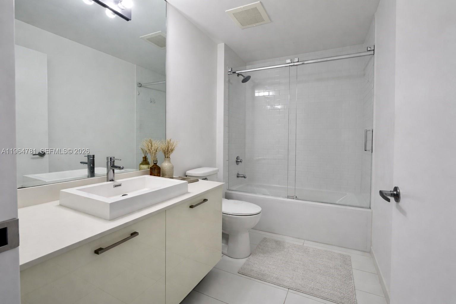 A modern bathroom features a white vanity, vessel sink, and a glass-enclosed shower-tub combination — 151 SE 1st St # 1501, Miami FL 33131, MIAMI, FL