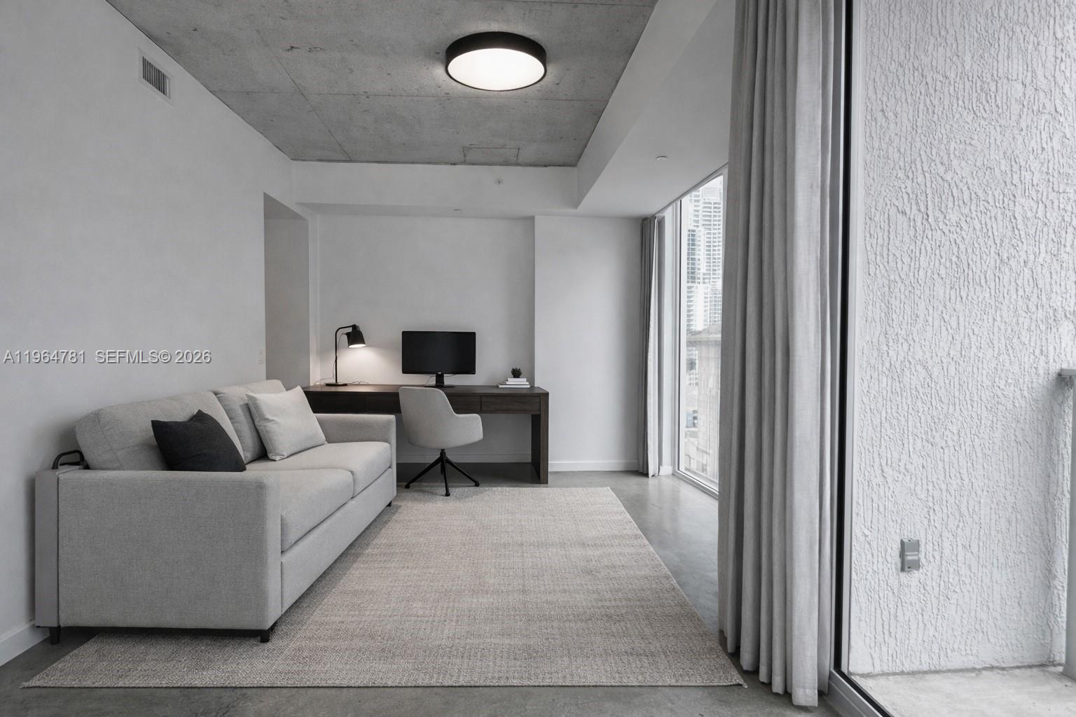 A modern room features a gray sofa, a desk with a computer, and concrete ceilings — 151 SE 1st St # 1501, Miami FL 33131, MIAMI, FL