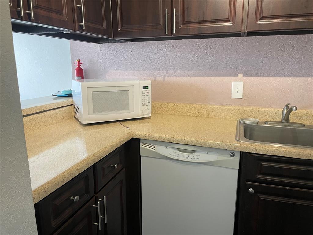 A kitchen features dark wood cabinets, a white stove, a window with blinds, and a refrigerator — 2625 STATE ROAD 590 UNIT 2711, CLEARWATER, FL