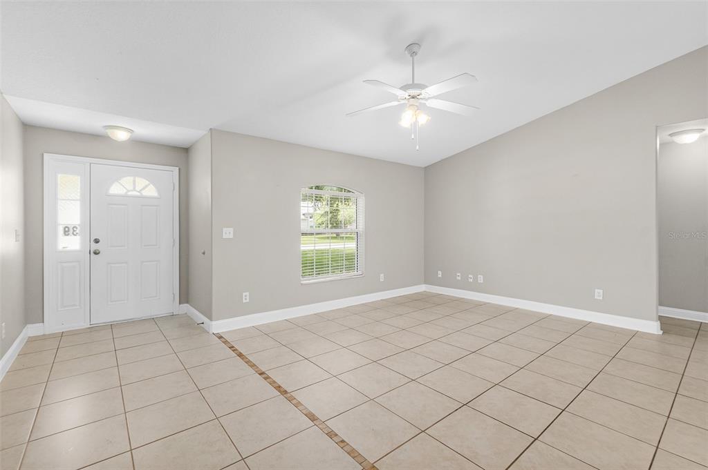 A bright living room features light-colored tile flooring, a ceiling fan, and an arched window — 39 PINWHEEL LANE, PALM COAST, FL