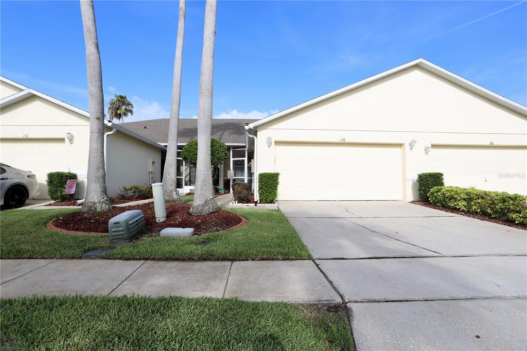 A beige single-story house with a two-car garage, palm trees, and a concrete driveway — 170 CLUB VILLAS LANE, KISSIMMEE, FL