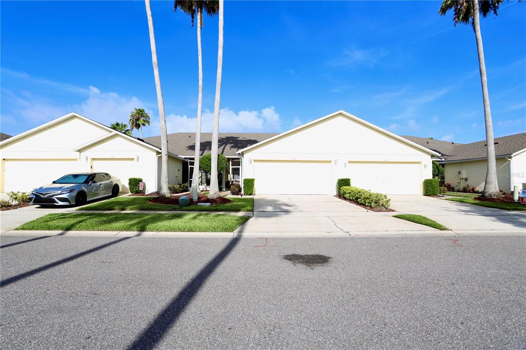 A street-level view of a light-colored duplex with two garages and palm trees — 170 CLUB VILLAS LANE, KISSIMMEE, FL