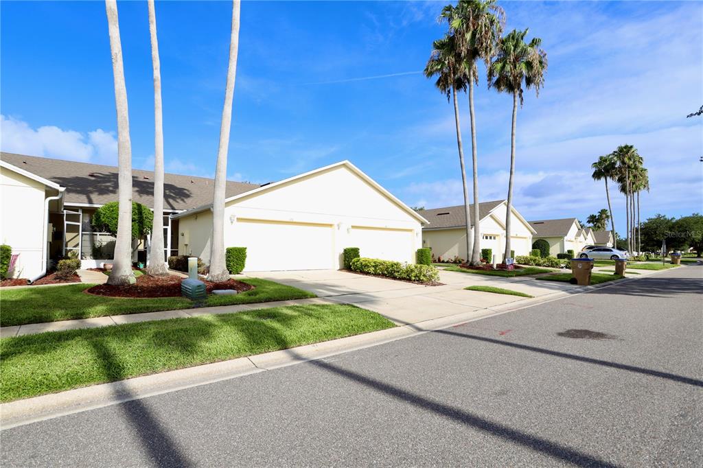 A street view of beige townhomes with attached garages and tall palm trees — 170 CLUB VILLAS LANE, KISSIMMEE, FL