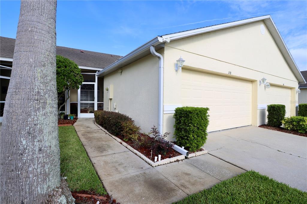 The exterior of a light-colored house features a garage, a walkway, and a screened entryway — 170 CLUB VILLAS LANE, KISSIMMEE, FL