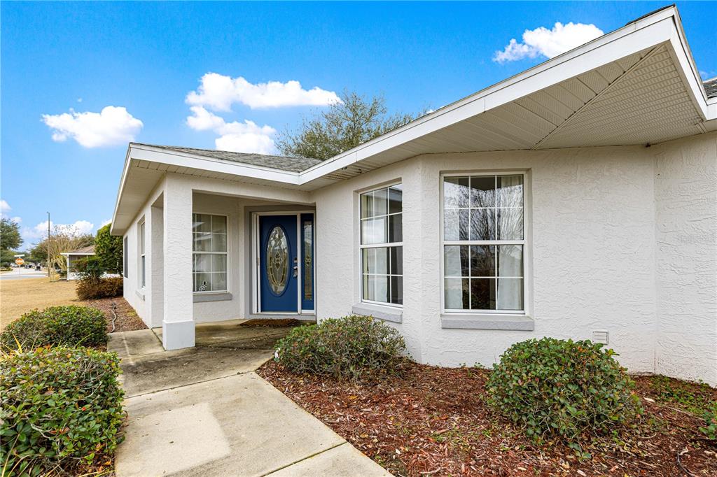 A white stucco house exterior features a blue front door and a concrete walkway — 9770 SW 92ND PLACE ROAD, OCALA, FL