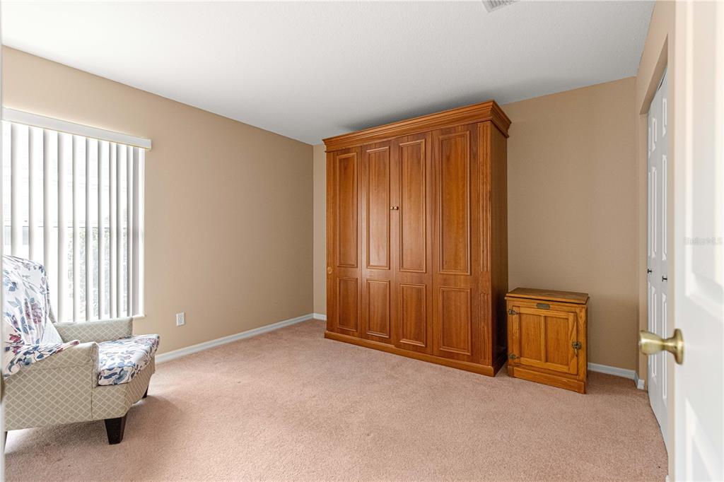 A bedroom features beige carpet, a large wooden wardrobe, and a patterned armchair by windows — 9770 SW 92ND PLACE ROAD, OCALA, FL