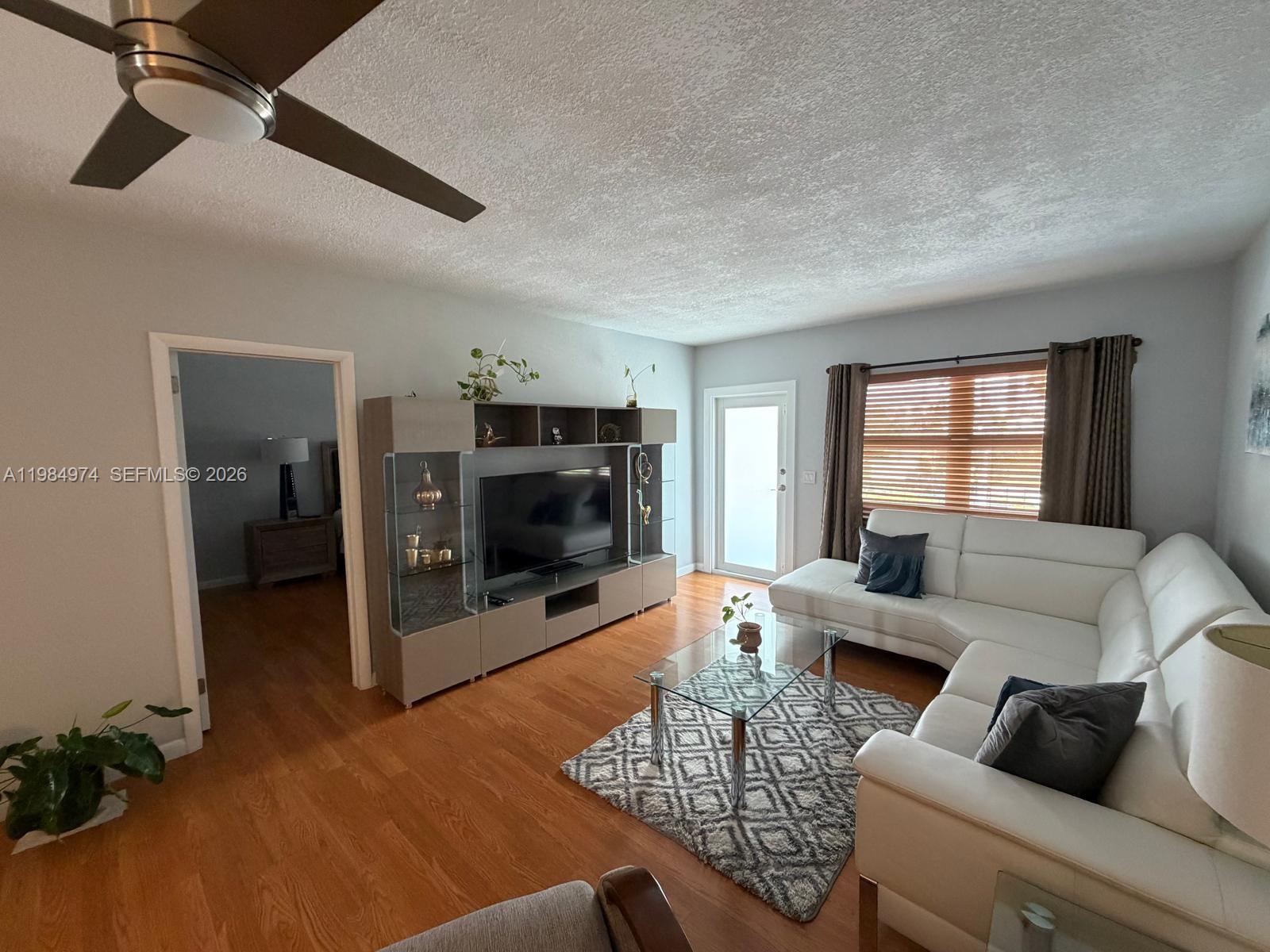 A living room features a white sectional sofa, a glass coffee table, and a media console — 630 Layne Blvd # 215, Hallandale Beach FL 33009, HALLANDALE BEACH, FL