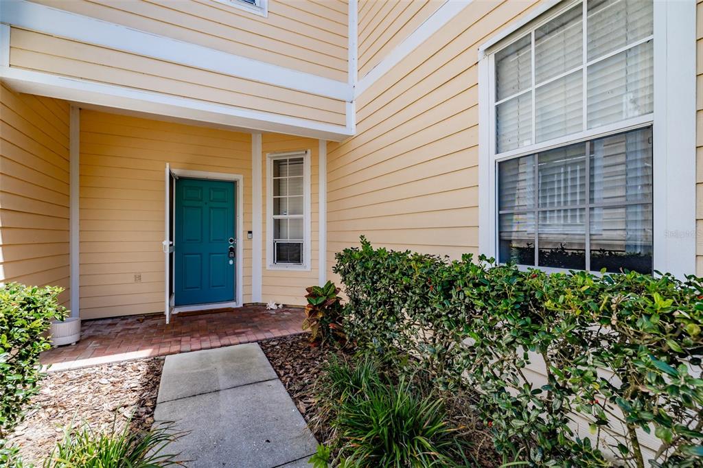 A teal front door is recessed into a yellow-sided building with a brick entryway — 6417 ROSEFINCH COURT UNIT 102, LAKEWOOD RANCH, FL