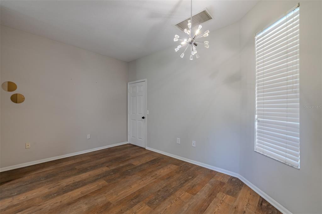 An empty room features wood-look flooring, light gray walls, a modern chandelier, and a window — 6417 ROSEFINCH COURT UNIT 102, LAKEWOOD RANCH, FL