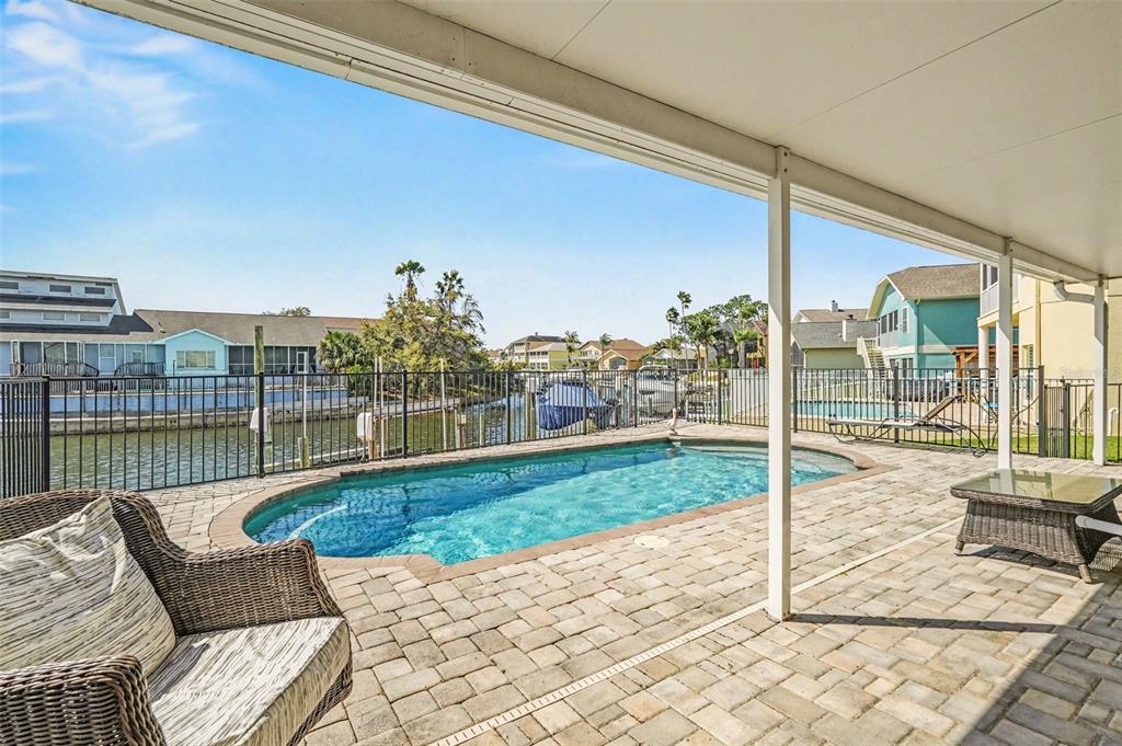 A covered patio overlooks a swimming pool and a canal with houses in the background — 6340 SPOONBILL DRIVE, NEW PORT RICHEY, FL
