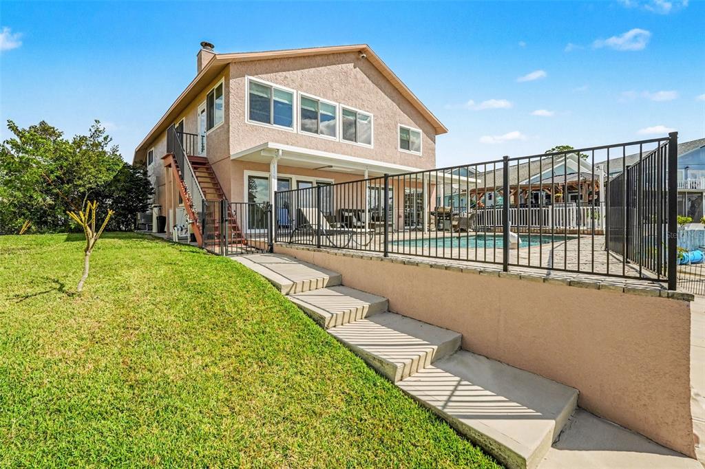 The exterior of a two-story house features a backyard pool, a metal fence, and stairs — 6340 SPOONBILL DRIVE, NEW PORT RICHEY, FL