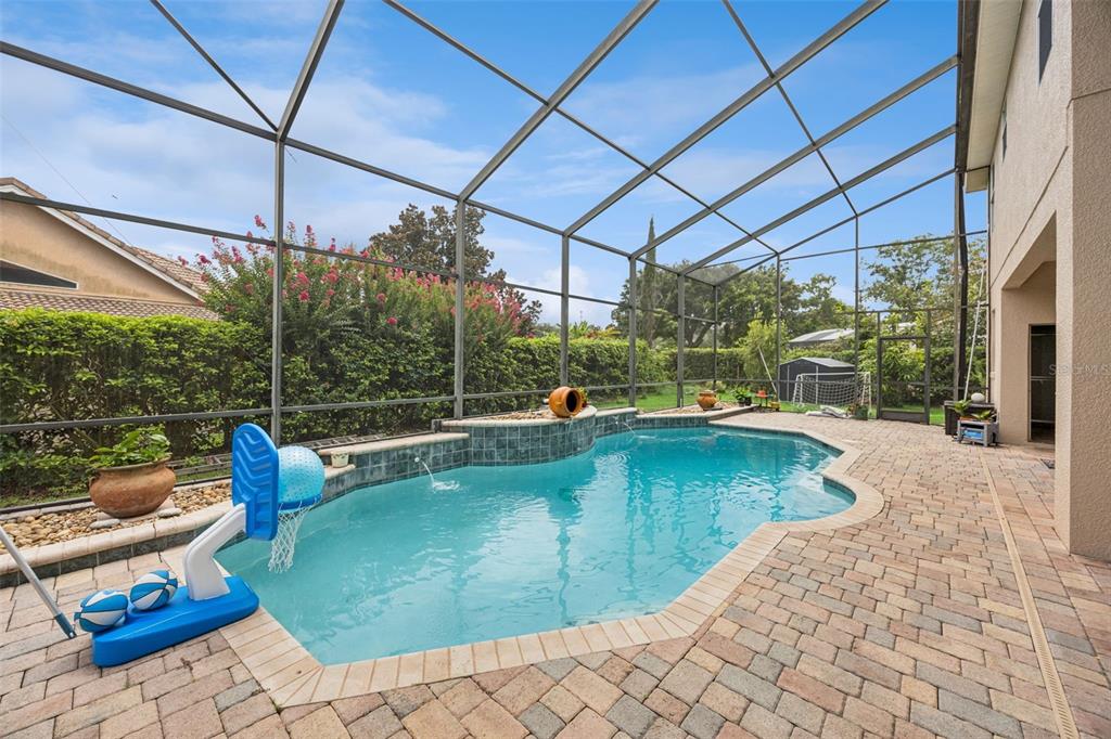 A screened-in patio features a swimming pool with a basketball hoop and paver decking — 8991 HERITAGE BAY CIRCLE, ORLANDO, FL