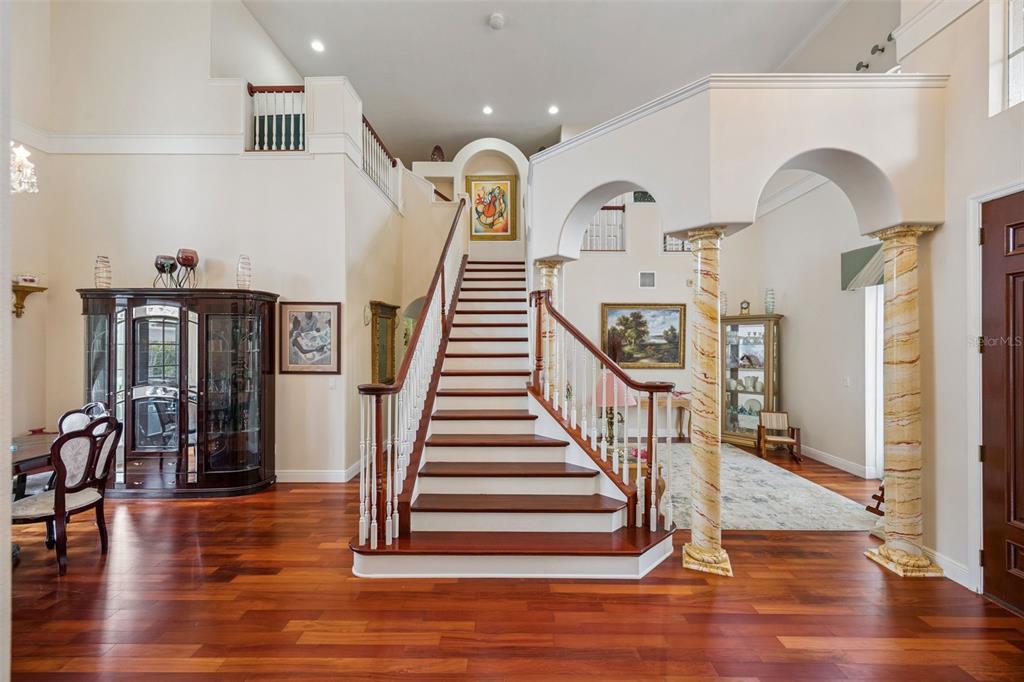 A grand foyer features a central staircase, marble-look columns, and hardwood flooring — 8991 HERITAGE BAY CIRCLE, ORLANDO, FL