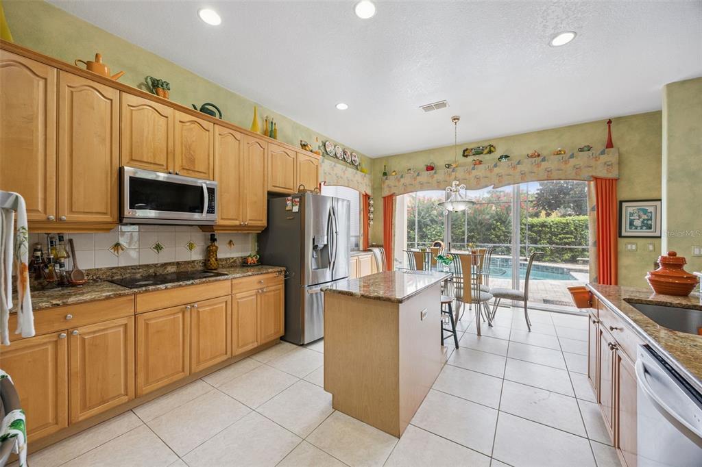 A kitchen with light wood cabinets, granite countertops, a center island, and a sliding glass door — 8991 HERITAGE BAY CIRCLE, ORLANDO, FL
