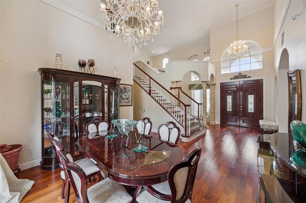 A formal dining room with a crystal chandelier, wooden table, and staircase in the background — 8991 HERITAGE BAY CIRCLE, ORLANDO, FL