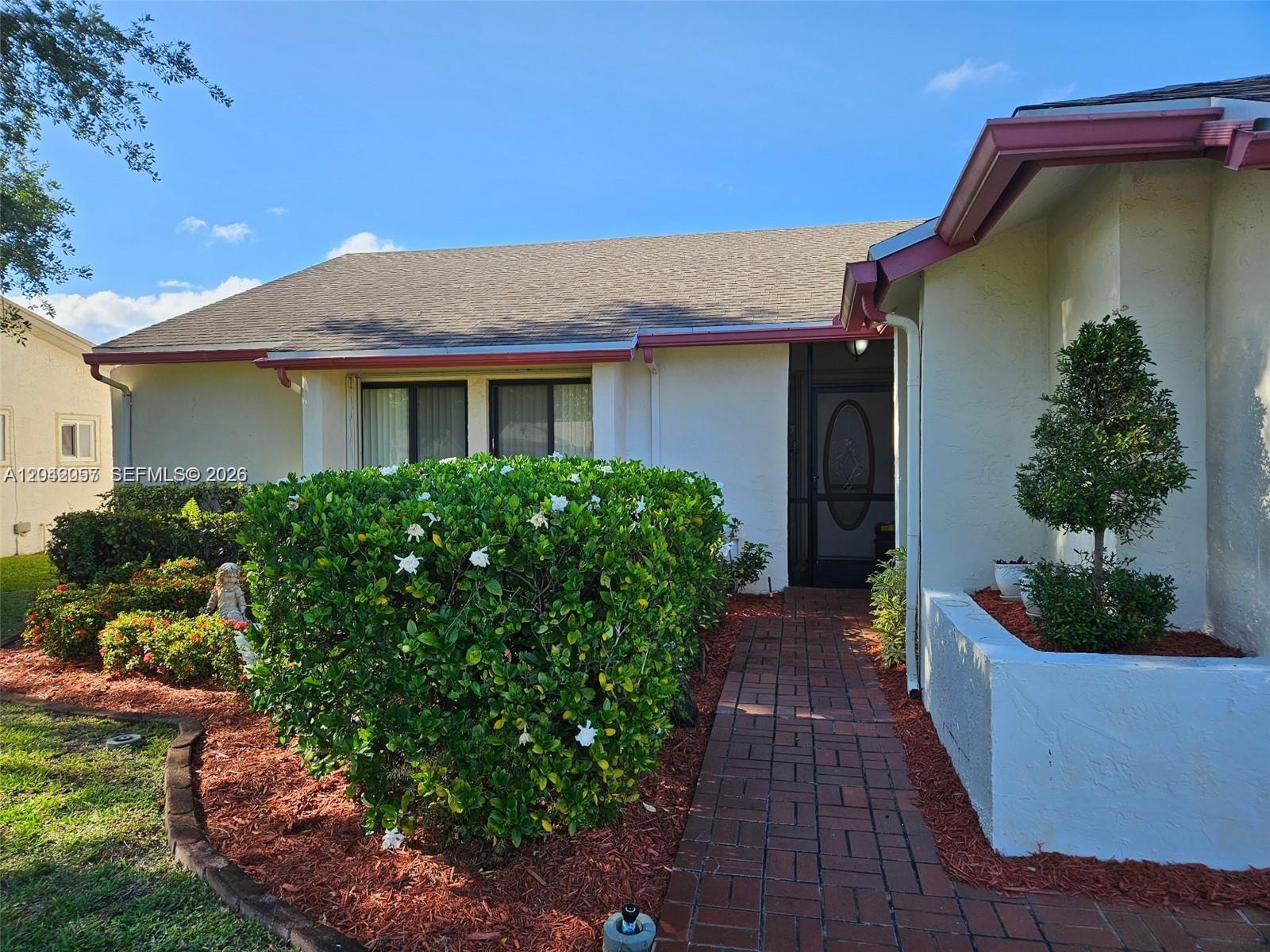 A brick walkway leads to the front entrance of a house with a large bush — 10301 Greenbriar Ct, Boca Raton FL 33498, BOCA RATON, FL