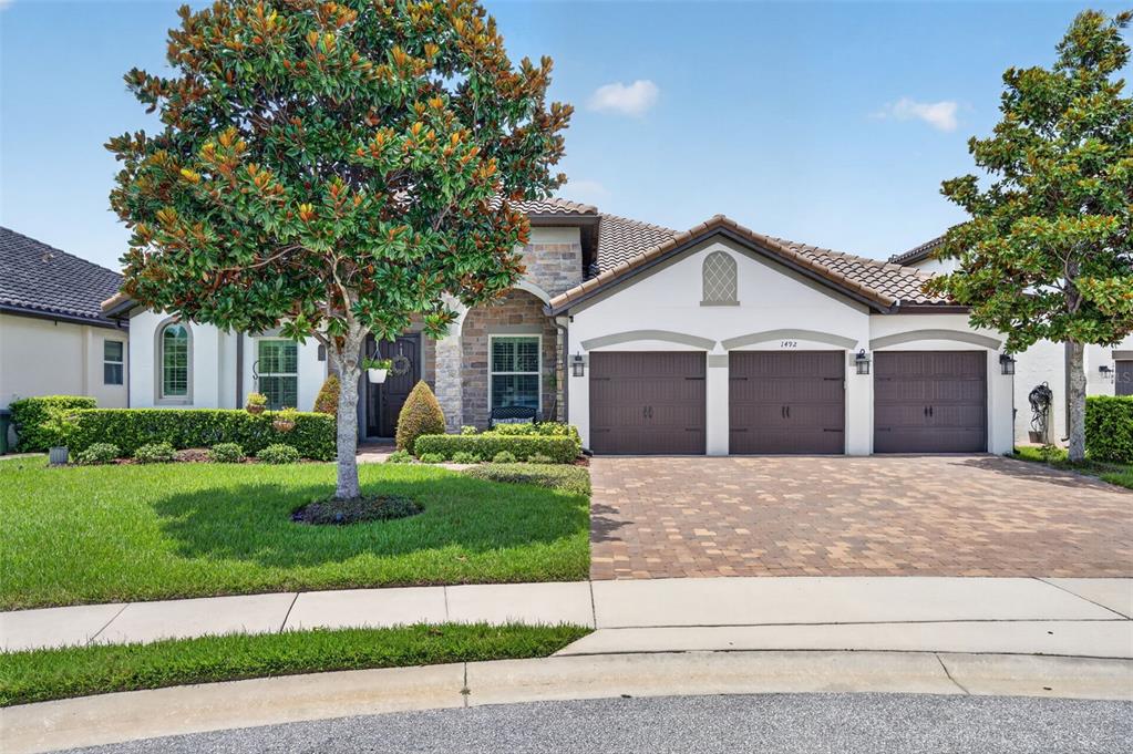 A single-story house with a three-car garage, stone accents, and a paved driveway — 1492 VIA SANGRO PL, WINTER PARK, FL