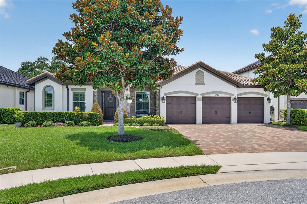 A single-story house with a three-car garage, a paved driveway, and a large front tree — 1492 VIA SANGRO PL, WINTER PARK, FL