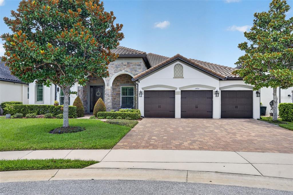 A single-story house with a stone facade, three garage doors, and a paved driveway — 1492 VIA SANGRO PL, WINTER PARK, FL