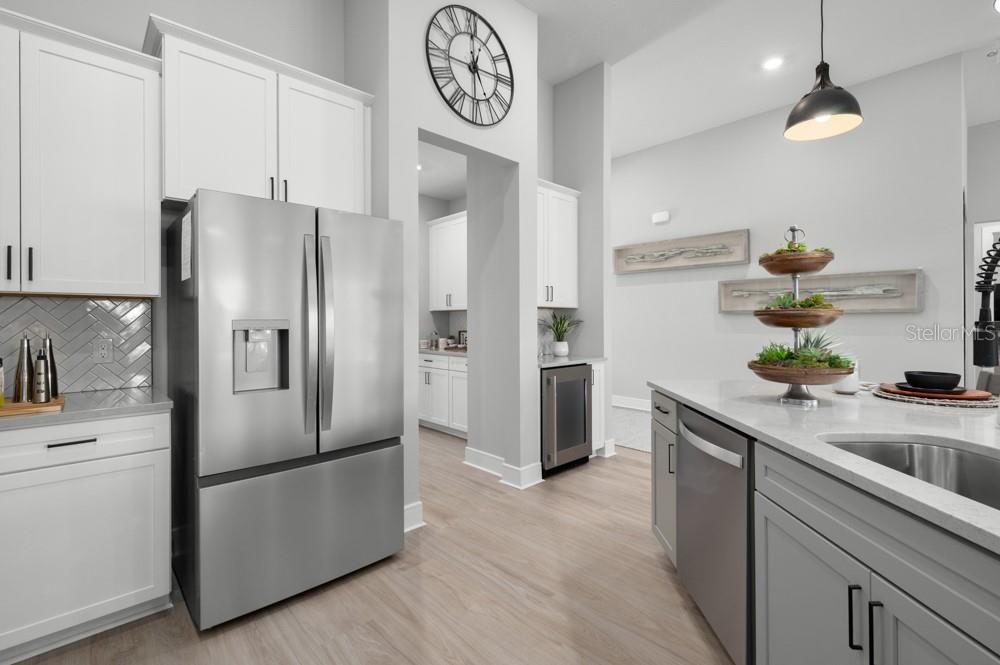 A modern kitchen features white cabinetry, stainless steel appliances, a gray island, and light flooring — 3832 SADDLE HILL TRAIL, FRUITLAND PARK, FL