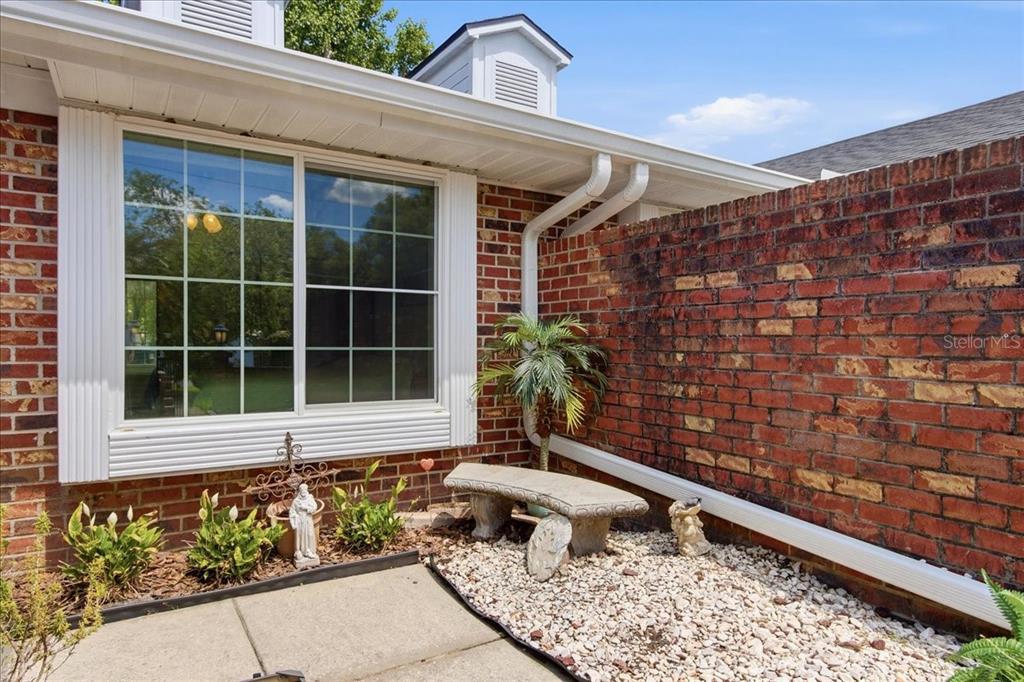 A brick exterior wall features a large window, a stone bench, and a gravel garden — 1429 S CHICKASAW TRAIL UNIT 7, ORLANDO, FL