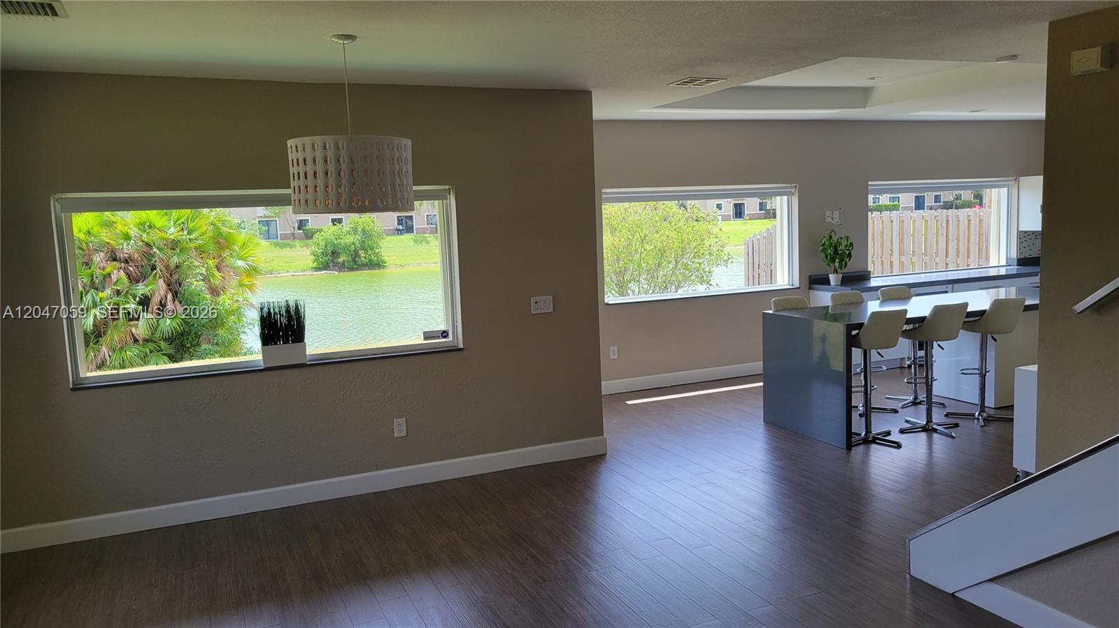 This open-concept living area features wood-look flooring, a kitchen island, and large waterfront windows — 8780 SW 223rd Ter # 8780, Cutler Bay FL 33190, CUTLER BAY, FL