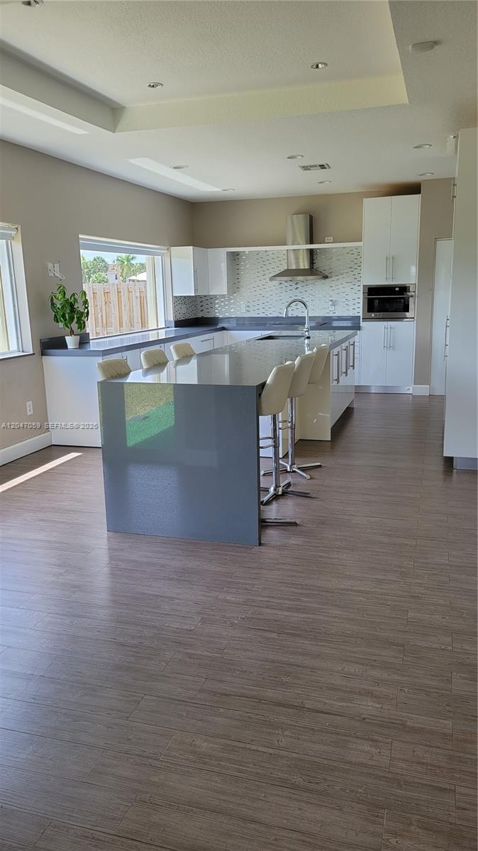 A modern kitchen features a gray waterfall island, white cabinetry, and wood-look flooring — 8780 SW 223rd Ter # 8780, Cutler Bay FL 33190, CUTLER BAY, FL
