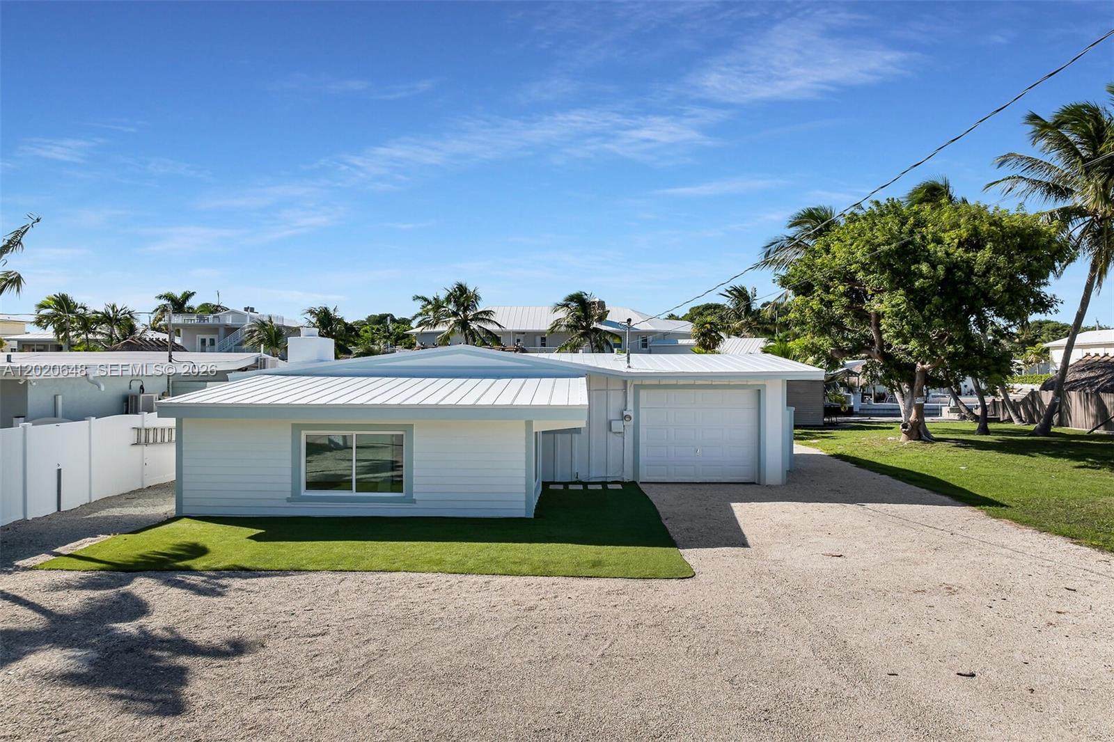 A single-story white house with a metal roof and a gravel driveway sits outdoors — 251 Azalea St, Plantation Key FL 33070, PLANTATION KEY, FL