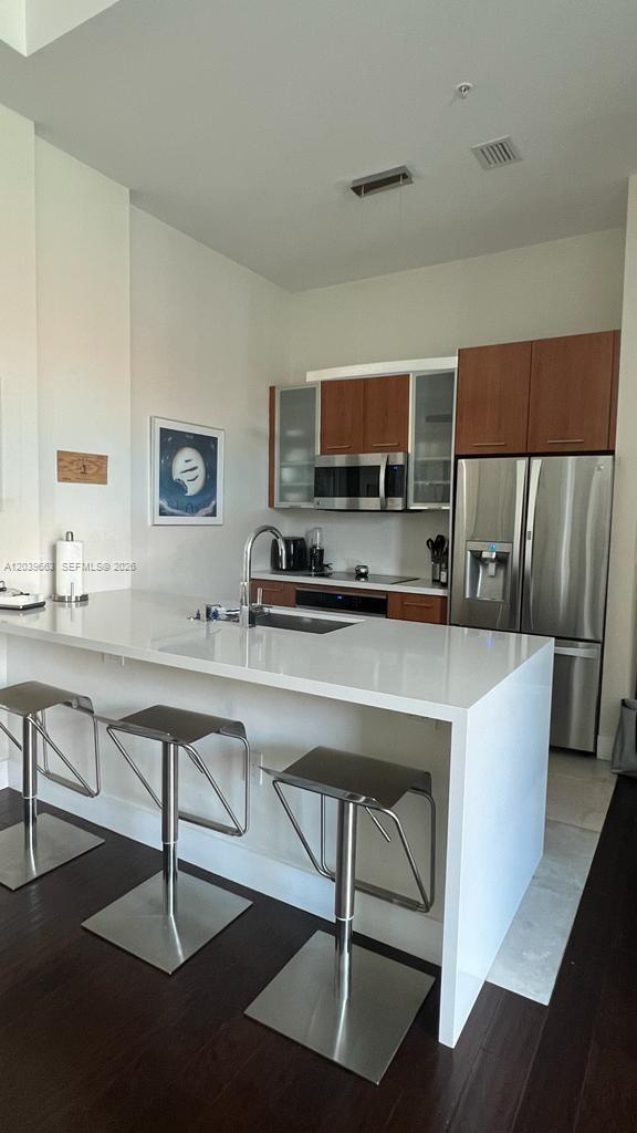 A kitchen features a white quartz island with three stools and wood-toned cabinetry — 9066 SW 73rd Ct # 607, Miami FL 33156, MIAMI, FL