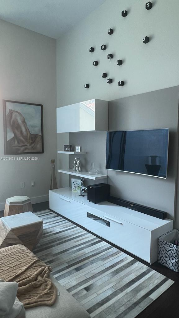 A modern living room features a wall-mounted television, white cabinetry, and a large wall clock — 9066 SW 73rd Ct # 607, Miami FL 33156, MIAMI, FL