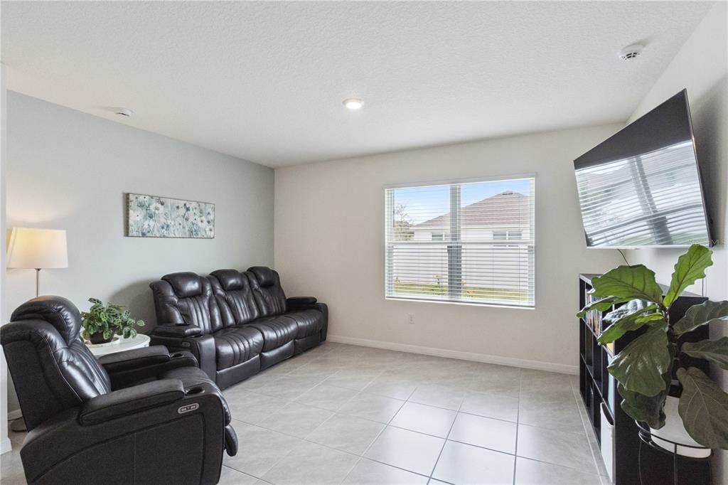 A living room features tile flooring, a black leather sofa, a recliner, and a wall-mounted television — 5825 ARBORETUM STREET, ST CLOUD, FL