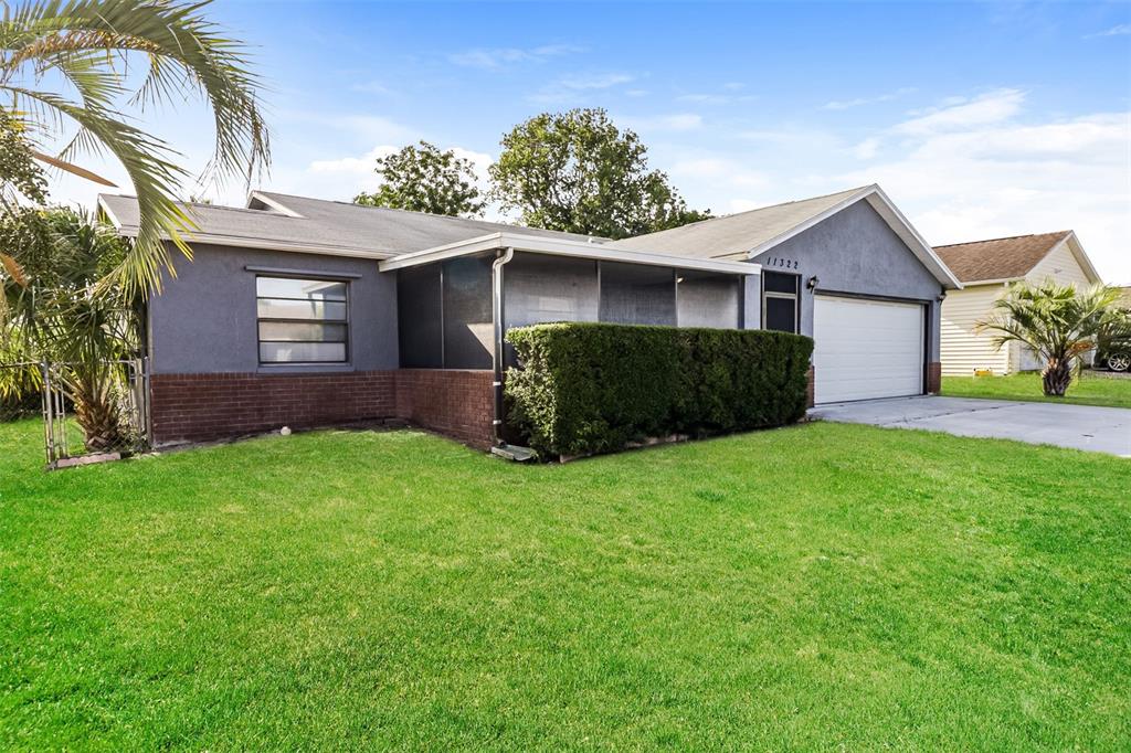 A single-story house with a gray exterior, brick base, screened porch, and attached garage — 11322 WOLF COURT, PORT RICHEY, FL